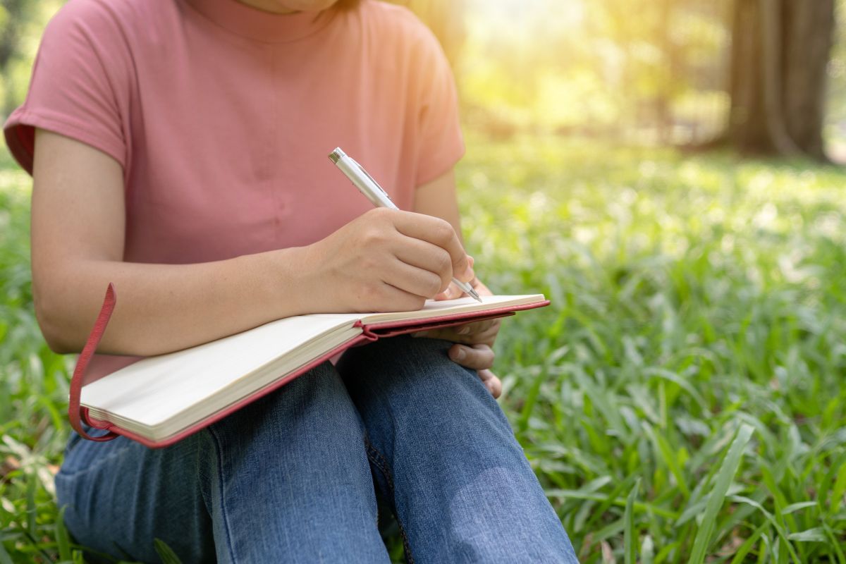 une femme qui écrit un poème d'amour à son amoureux, assise sur l'herbe