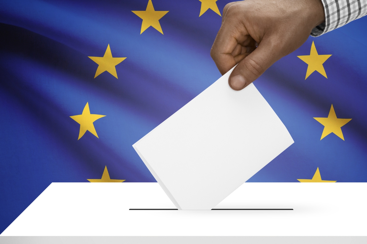 Une main qui vote en glissant un bulletin dans une urne avec le drapeau européen en arrière plan