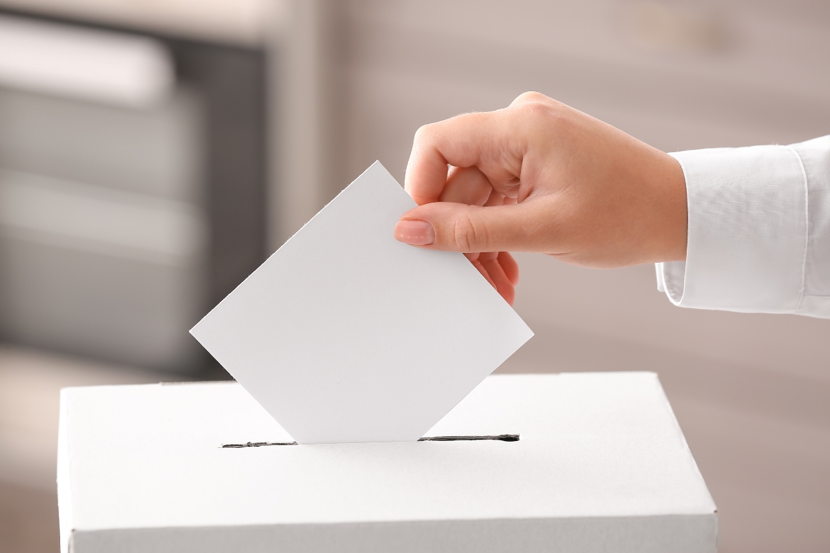 Une main qui vote en glissant un bulletin de vote dans une urne