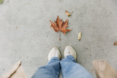 Femme en jean pattes delephant avec une feuilel au sol symbolisant lautomne