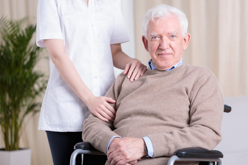 une aide à domicile épaule un homme en fauteuil roulant