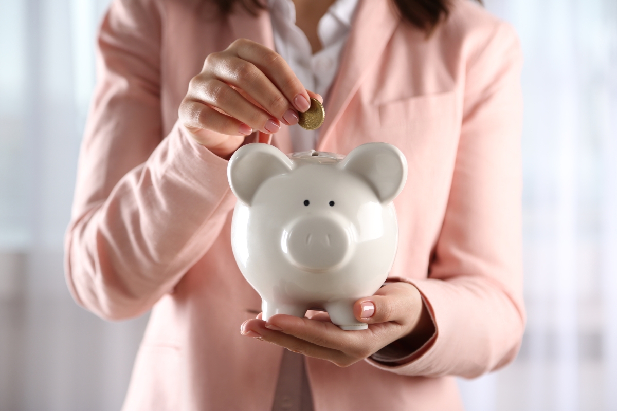 une femme qui met une piece dans une tirelire en forme de cochon