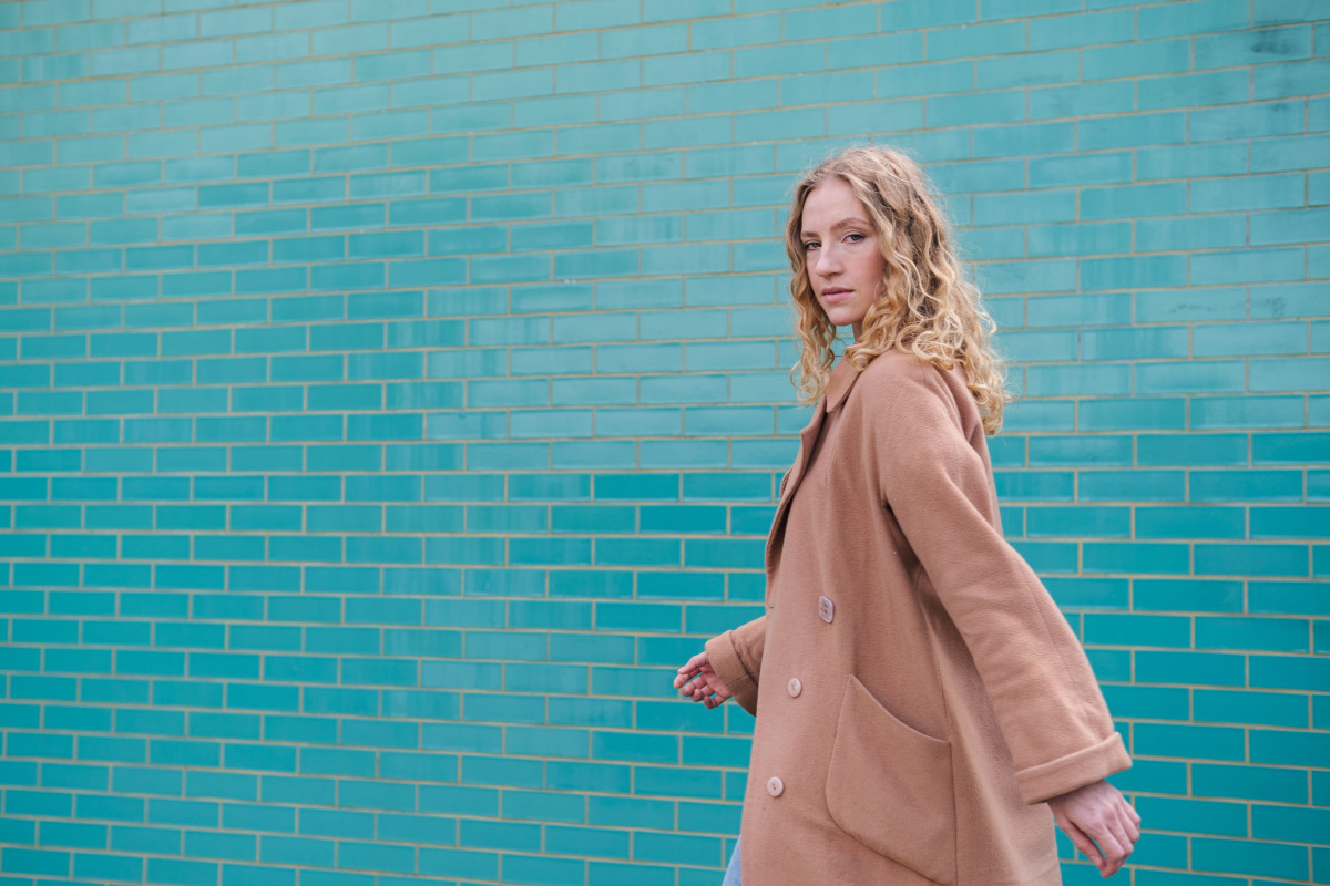 Une femme en long manteau marche à nouveau avec un regard de défi