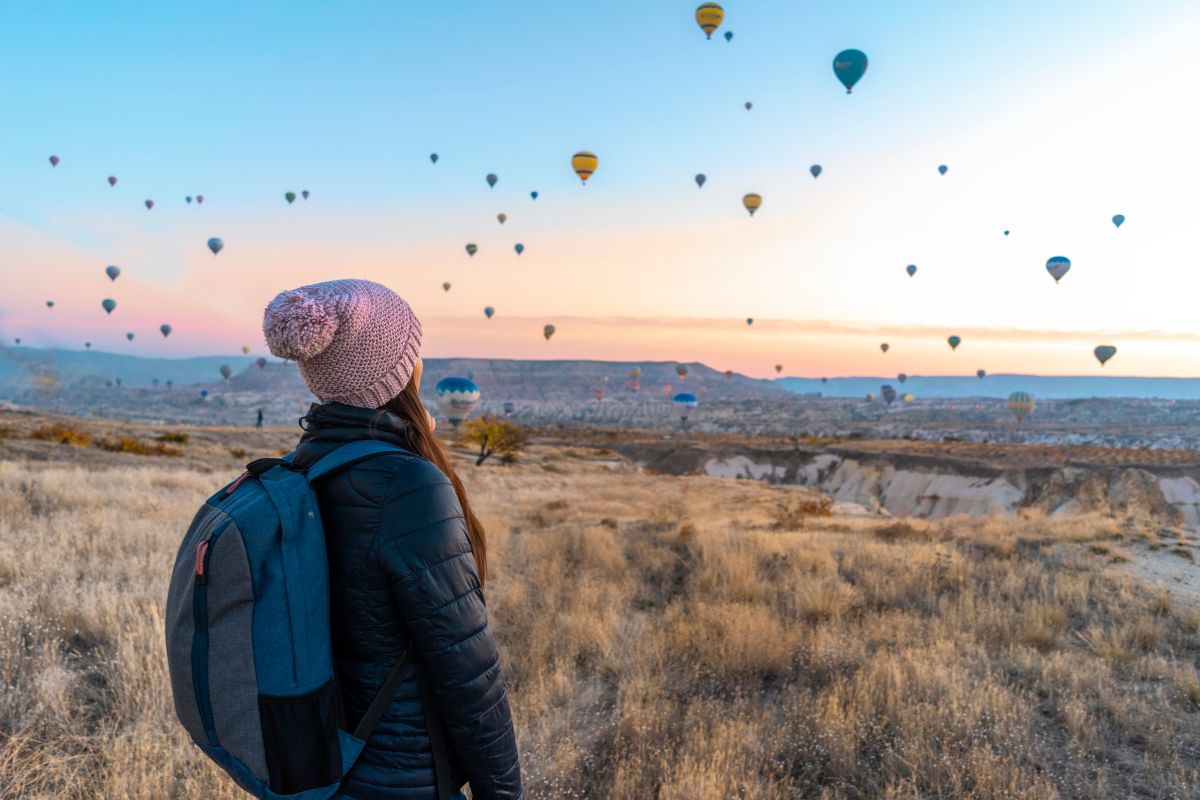 une femme en voyage vacance qui regarde des dizaines de montgolfières dans le ciel dans un paysage somptueux