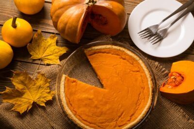 une ^délicieuse tarte à la citrouille végan servie dans un décor automnal composé de citrouilles et de feuilles mortes