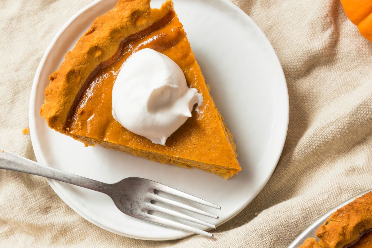 une délicieuse part de tarte à la citrouille végan servi dans un plat, recouverte d'une belle creme végétarienne