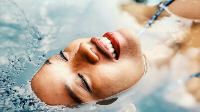 une femme sur le dos dans l'eau la tête à moitié immergée, fermant les yeux, en pleine cure bien être