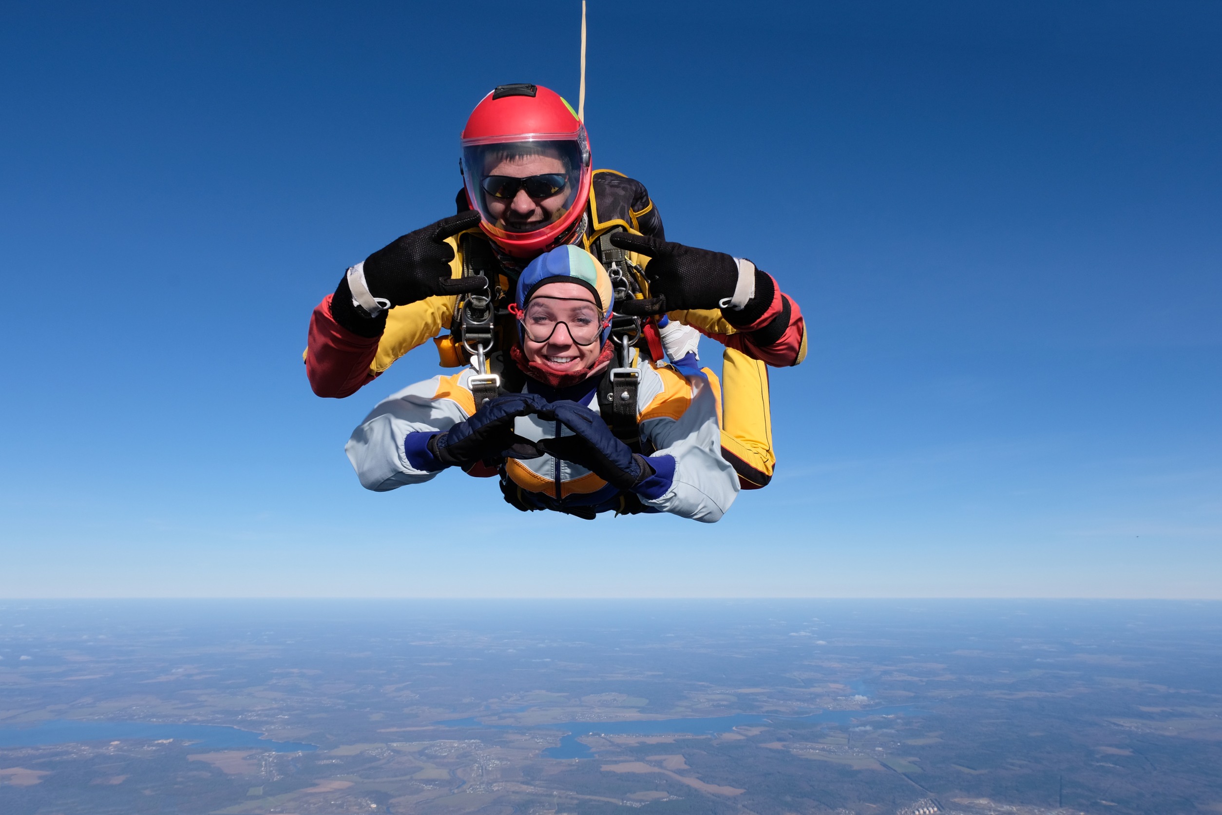 Une femme gros sourire fait un signe de coeur avec ses mains en plein saut en parachute accompagne de son moniteur superbe paysage