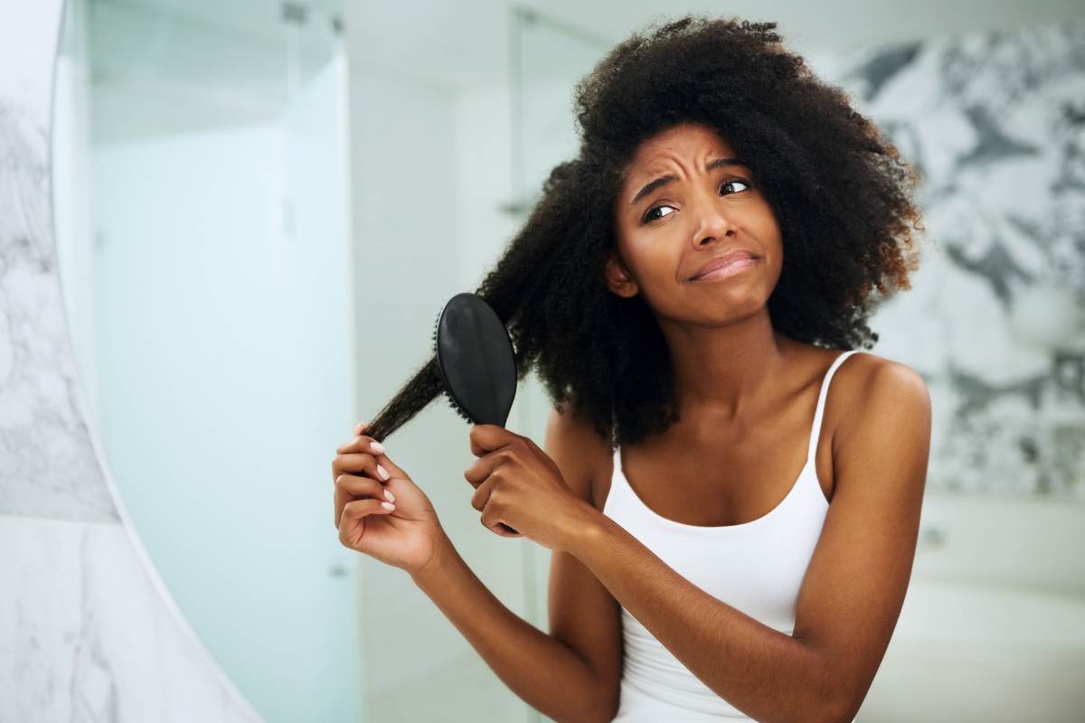 une femme noire triste aux cheveux crépus qui essaie de coiffer ses cheveux trop secs