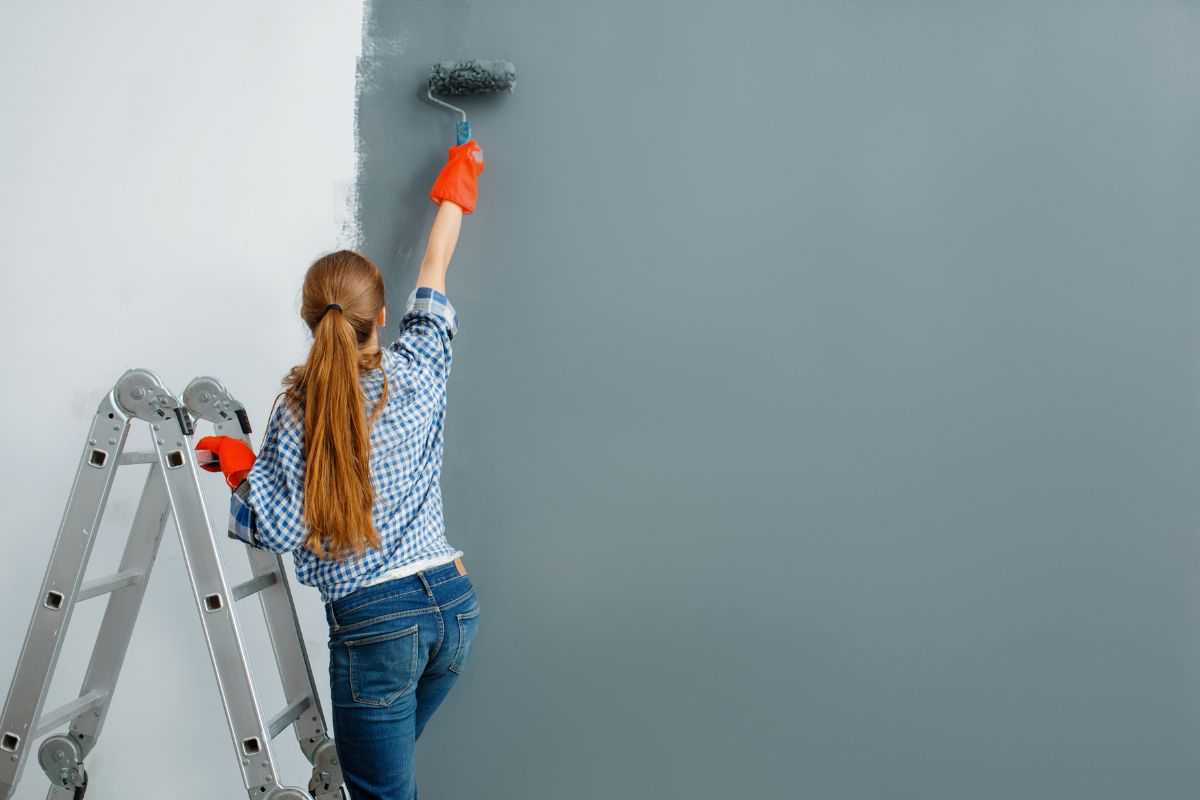 une femme peint son mur en une couleur tendance pour 2025 sur un escabeau, nouvelles idées déco salon maison